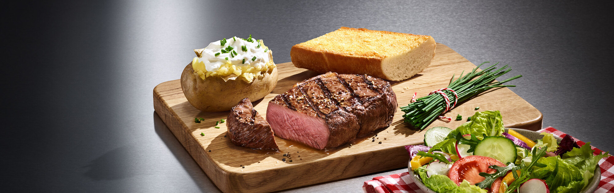 Ein saftiges Steak, eine gefüllte Ofenkartoffel und ein knuspriges Stück Brot auf einem Holzbrett