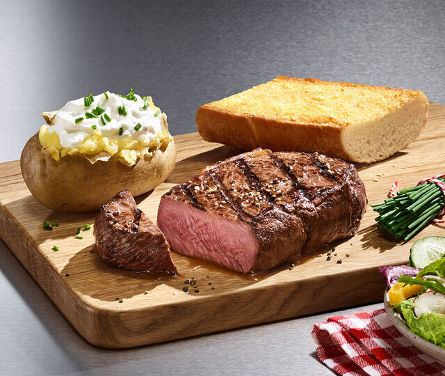 Ein saftiges Steak, eine gefüllte Ofenkartoffel und ein knuspriges Stück Brot auf einem Holzbrett