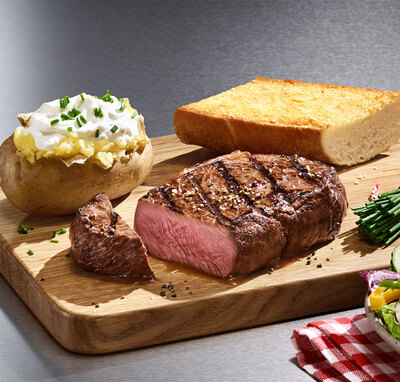 Ein saftiges Steak, eine gefüllte Ofenkartoffel und ein knuspriges Stück Brot auf einem Holzbrett