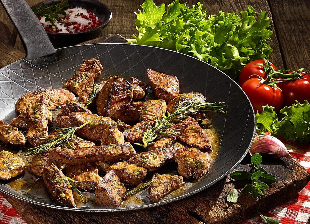 Kleingeschnittenes Fleisch in einer Pfanne angerichtet mit Kräutern.