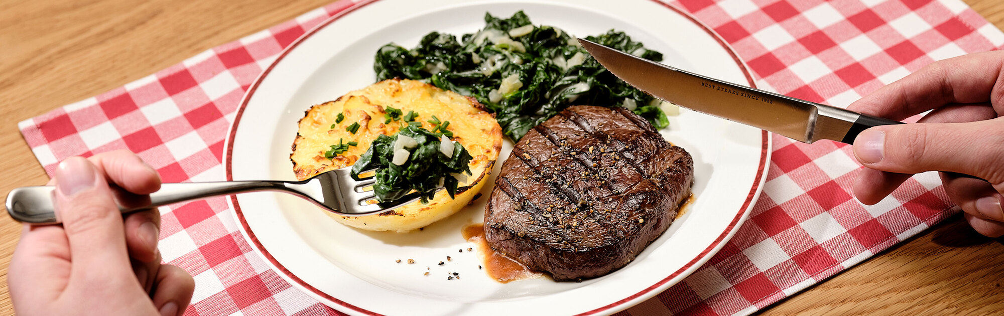 Saftig gegrilltes Rindersteak, serviert mit cremigem Kartoffelgratin und frischem Blattspinat auf einem Teller, platziert auf einer rot-weiß karierten Tischdecke.