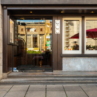 Eingang des BLOCK HOUSE Stuttgart Arnulf-Klett-Platz mit Menütafel vor dem Steakhouse und Gästen an Tischen mit rot-weiß karierten Tischdecken