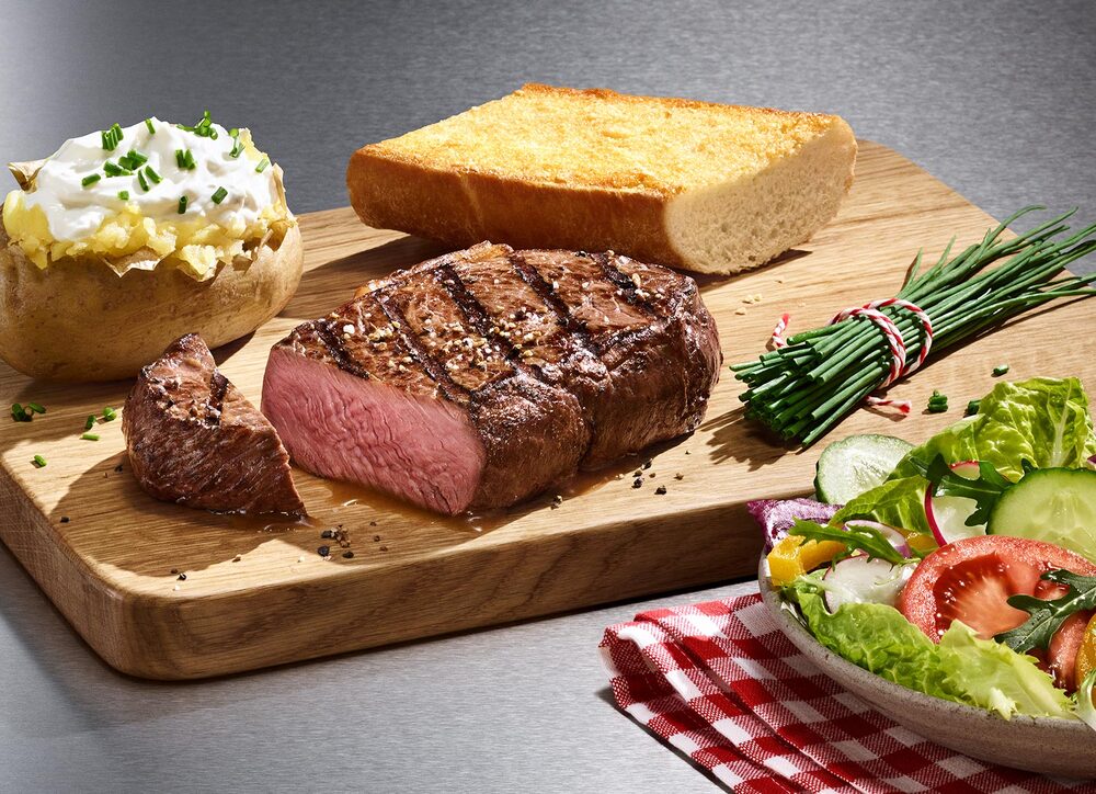 Steak, Baked Potato und BLOCK HOUSE Brot auf einem Holzbrett, serviert mit einem BLOCK HOUSE Salat 