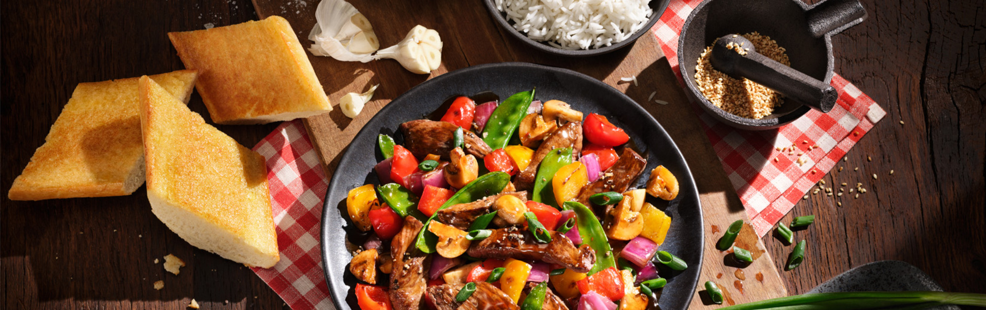 BLOCK HOUSE Teriyaki Steak Pfanne frisch zubereitet in einer Pfanne daneben BLOCK HOUSE Knoblauchbrot.