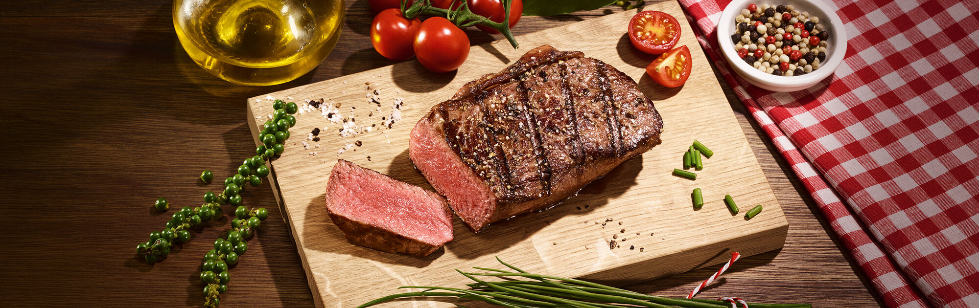 Angeschnittenes Steak auf einem Holzbrett angerichtet mit Kräutern und Tomaten.