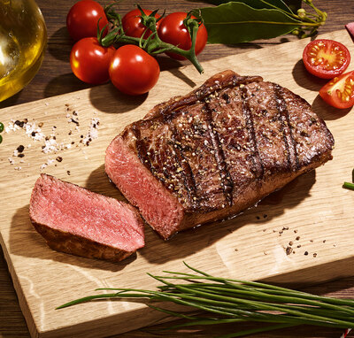 Angeschnittenes Steak auf einem Holzbrett angerichtet mit Kräutern und Tomaten.