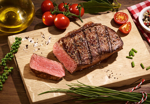 Angeschnittenes Steak auf einem Holzbrett angerichtet mit Kräutern und Tomaten.