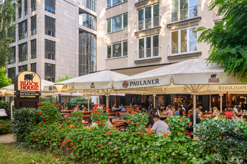 Sonnengeschützte Terrasse des BLOCK HOUSE München Leopoldstraße mit Gästen und Sonnenschirmen vor dem Steakhouse