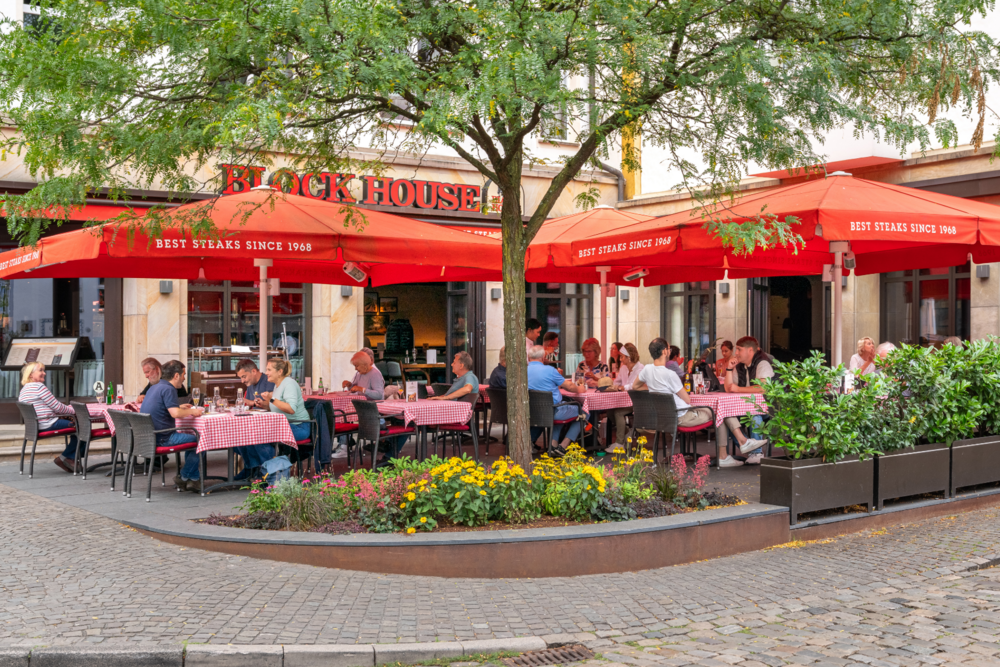Terrasse des BLOCK HOUSE Bielefeld mit roten Sonnenschirmen und Gästen im Außenbereich.