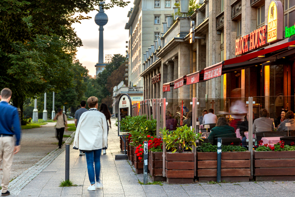 Außenansicht des BLOCK HOUSE Berlin an der Karl-Marx-Allee mit Terrasse und Gästen am Boulevard.