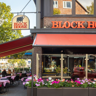 Außenansicht des BLOCK HOUSE Hamburg Barmbek mit Terrasse, roten Markisen und Sitzplätzen vor dem Steakhouse