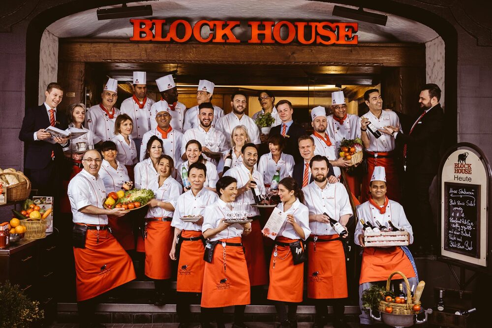 Gruppenfoto der Mitarbeiter des BLOCK HOUSE Restaurants in der Kirchenallee in Hamburg vor dem Eingang des Restaurants