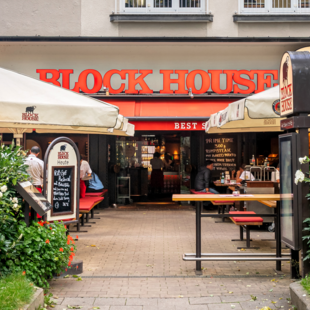 Eingang und Terrasse des BLOCK HOUSE München Leopoldstraße mit Sonnenschirmen und Gästen vor dem Steakhouse