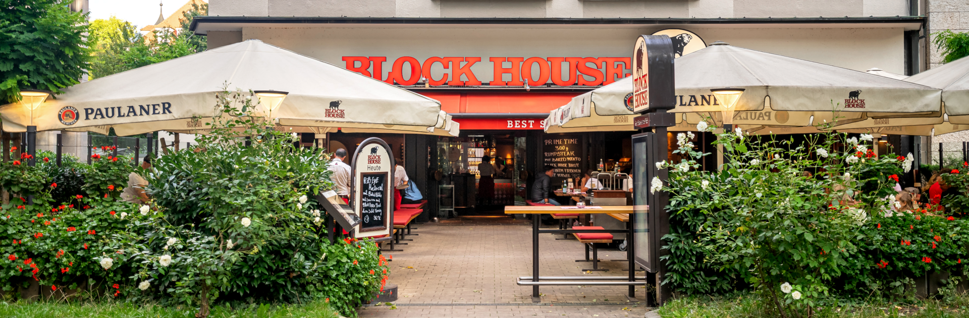 Eingang und Terrasse des BLOCK HOUSE München Leopoldstraße mit Sonnenschirmen und Gästen vor dem Steakhouse